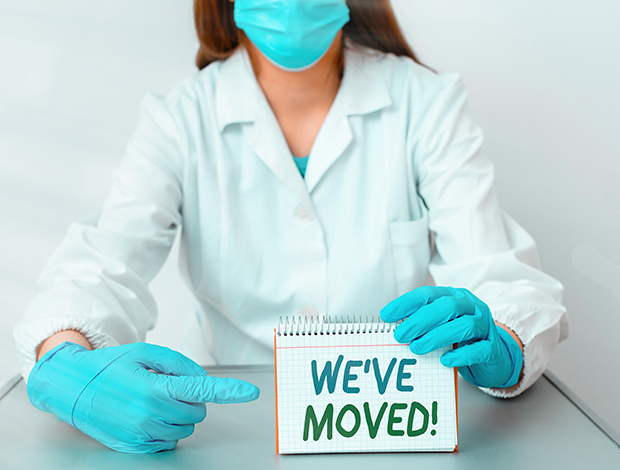 Lab worker holding a sign that says We've Moved