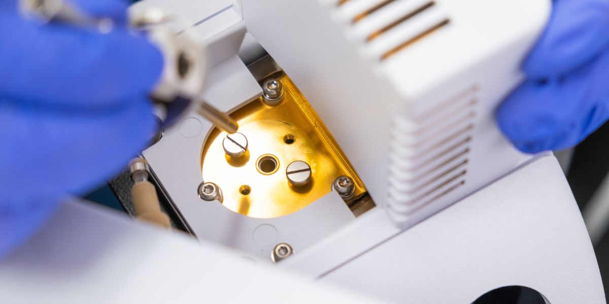 Close-up of a laboratory technician using gloved hands to maintain a mass spectrometer